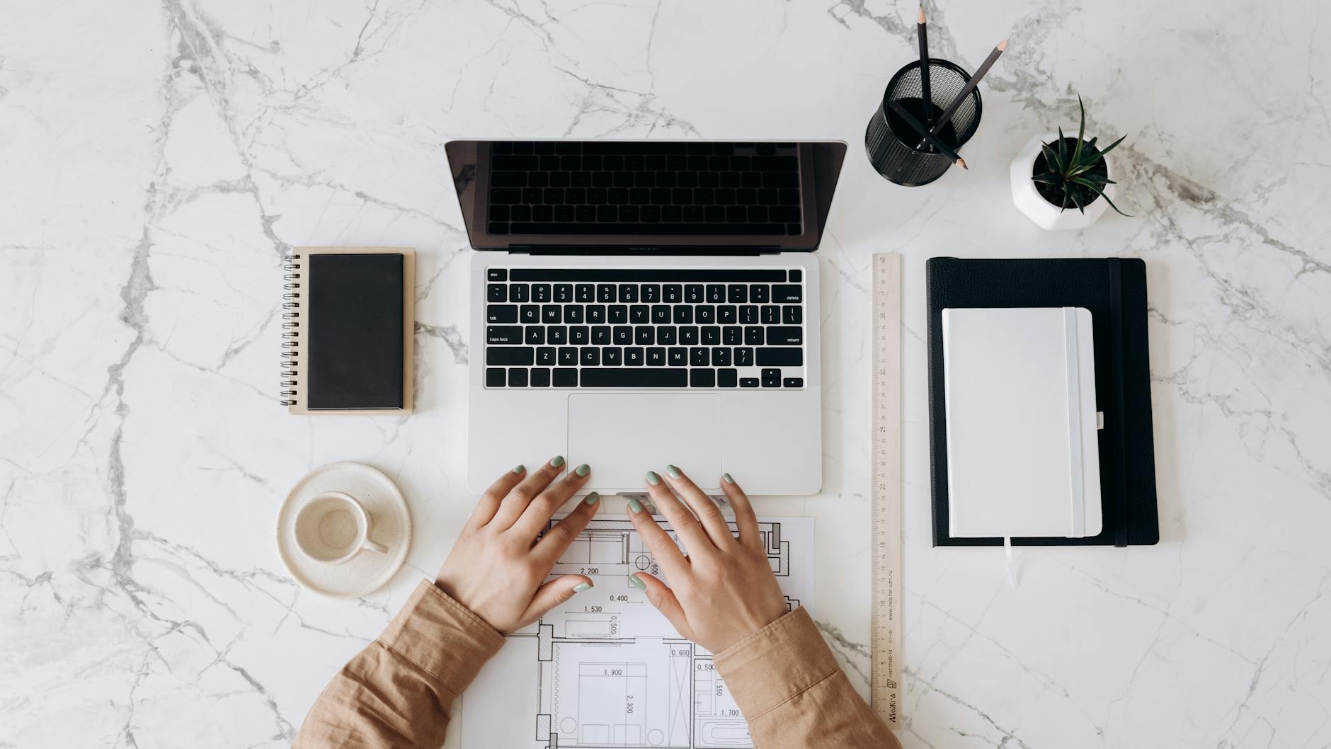 person in brown long sleeve shirt using macbook pro beside white ceramic mug