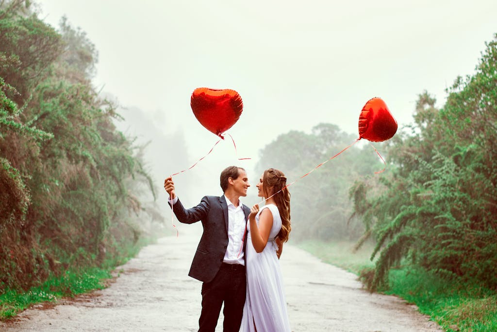 A loving couple embraces with heart-shaped balloons in a foggy park setting.